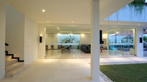A modern house with a glass-enclosed living area, a staircase, and a well-lit interior. - Villa Aquila Seminyak (Seminyak)