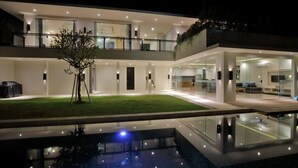 A modern two-story house with a glass facade, a swimming pool, and a well-lit outdoor area. - Villa Aquila Seminyak (Seminyak)