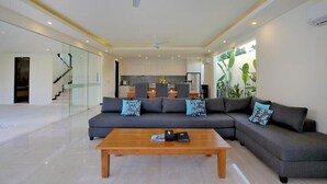 A modern living room with a sectional sofa, a wooden coffee table, and a kitchen in the background. - Villa Aquila Seminyak (Seminyak)