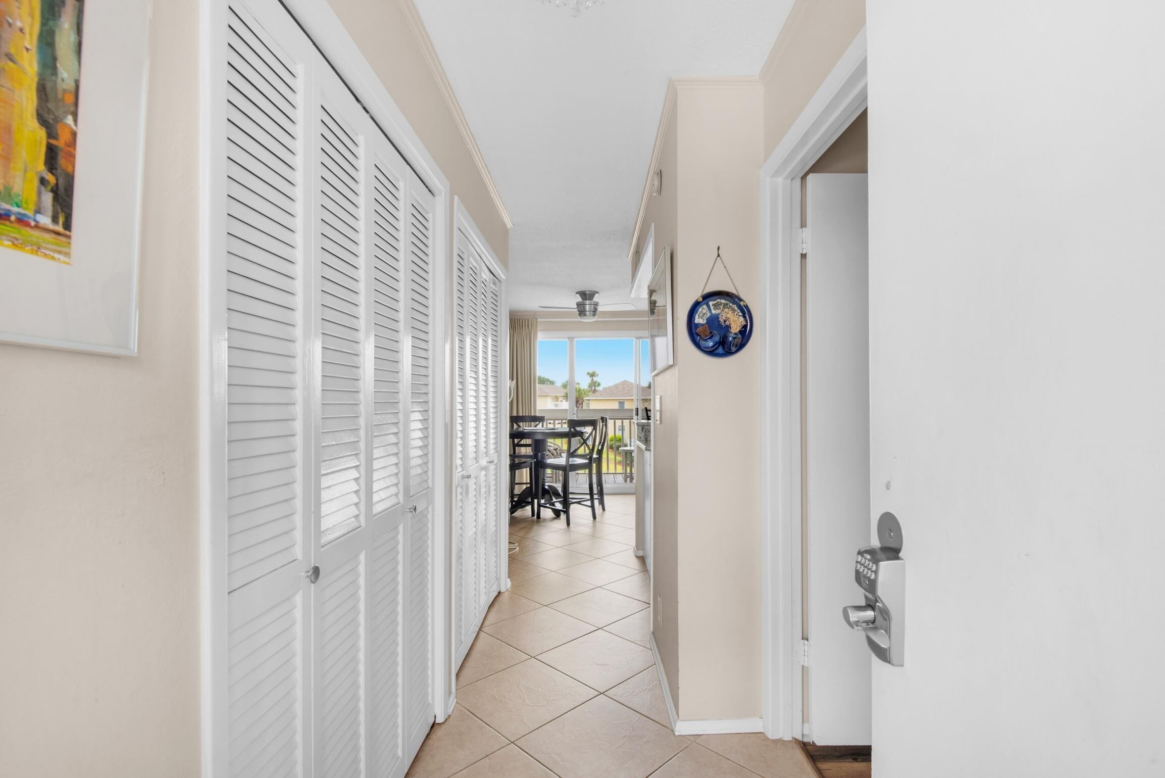 A hallway with white doors, a dining area with a table and chairs, and a view of the outside.