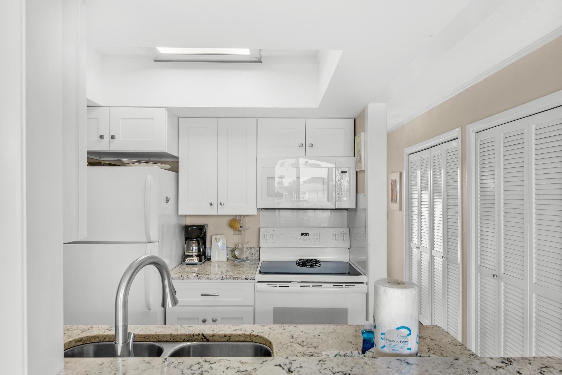 A compact kitchen with white cabinets, a stainless steel sink, a built-in stove, and a countertop with a roll of paper towels.