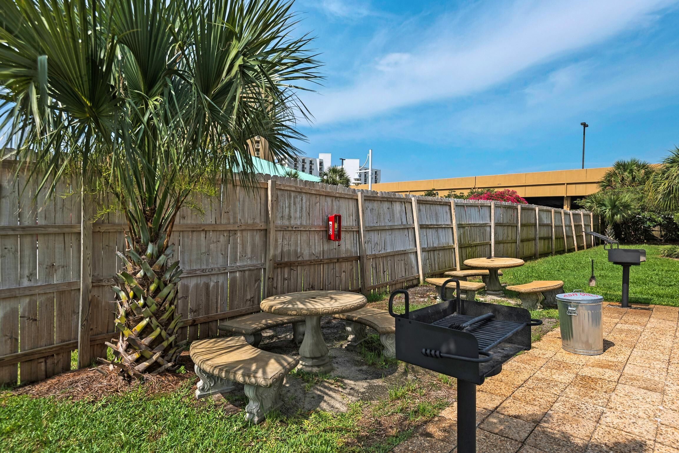 Eine Terrasse im Freien mit Grill, Steintischen und einem Holzzaun.