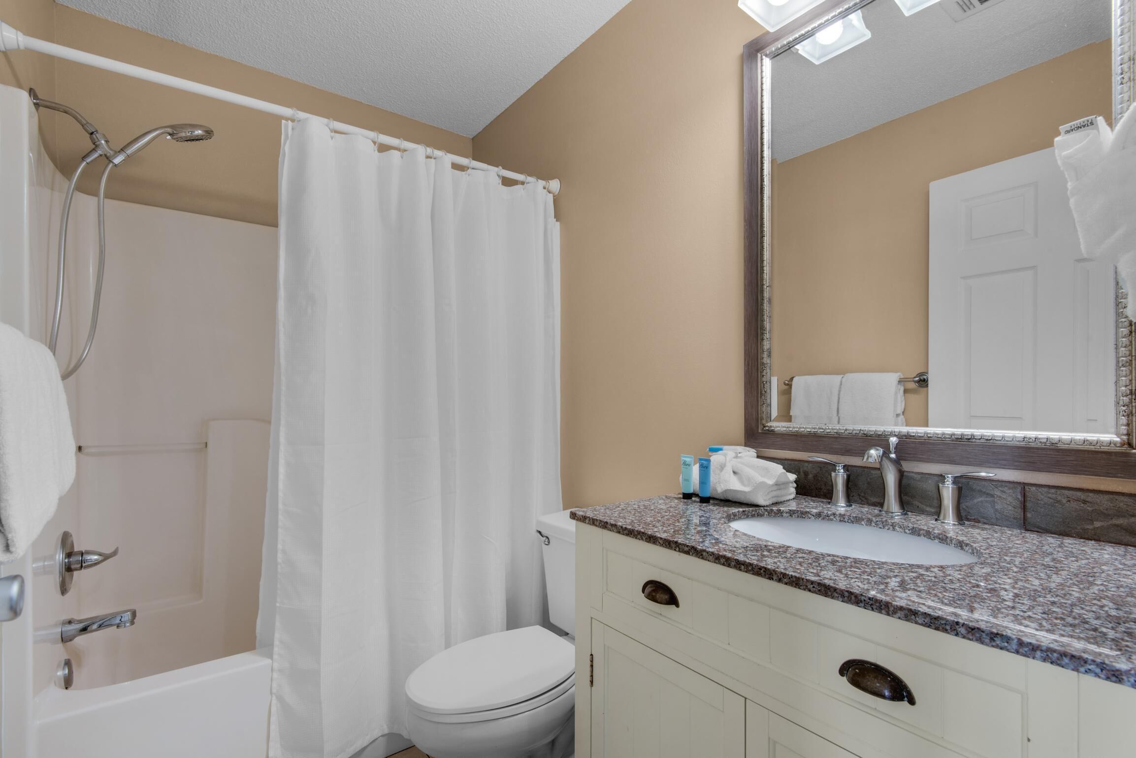 A bathroom with a shower, toilet, sink, and mirror.