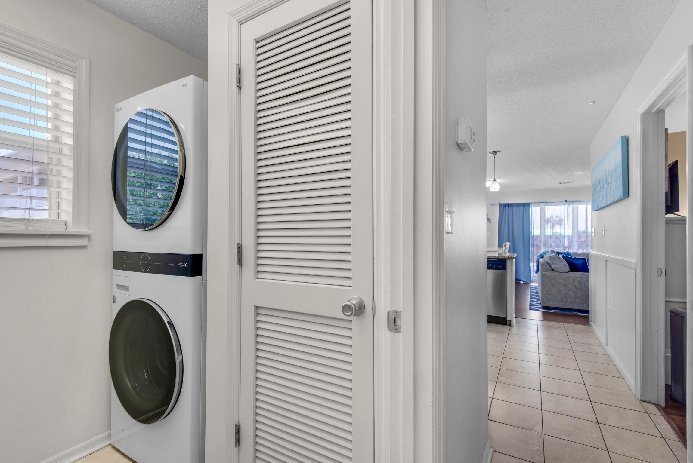 Une buanderie équipée d’un lave-linge et d’un sèche-linge à chargement frontal, d’une porte à panneaux ajourés et d’un couloir menant à un espace de vie comprenant un canapé et un coin repas.