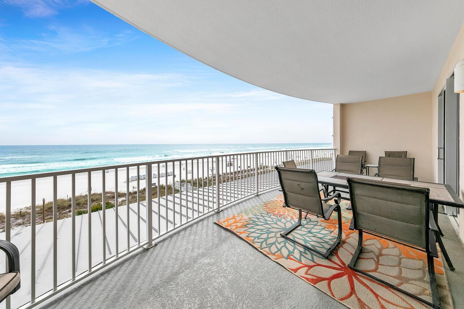 A balcony with a view of the ocean, a table with chairs, and a patterned rug.