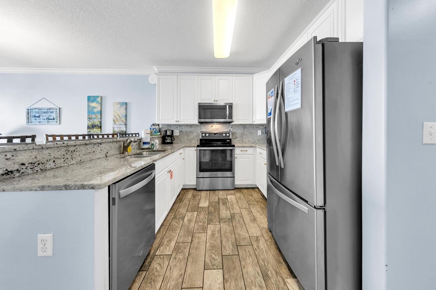 A modern kitchen with stainless steel appliances, white cabinetry, and a wooden floor.