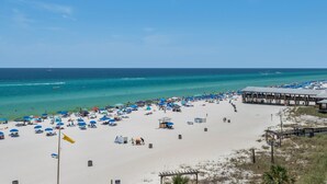 Een strand met parasols, ligbedden en een pier.