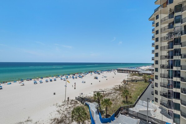 A beach with a pier, a high-rise building, and a clear blue sky.