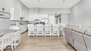 A modern kitchen with white cabinetry, a dining area with white chairs, and a grey sofa. - Pelican at Sound Side (Fort Walton Beach)