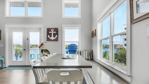 A dining area with a long table, white chairs, and a view of the outdoors. - Pelican at Sound Side (Fort Walton Beach)
