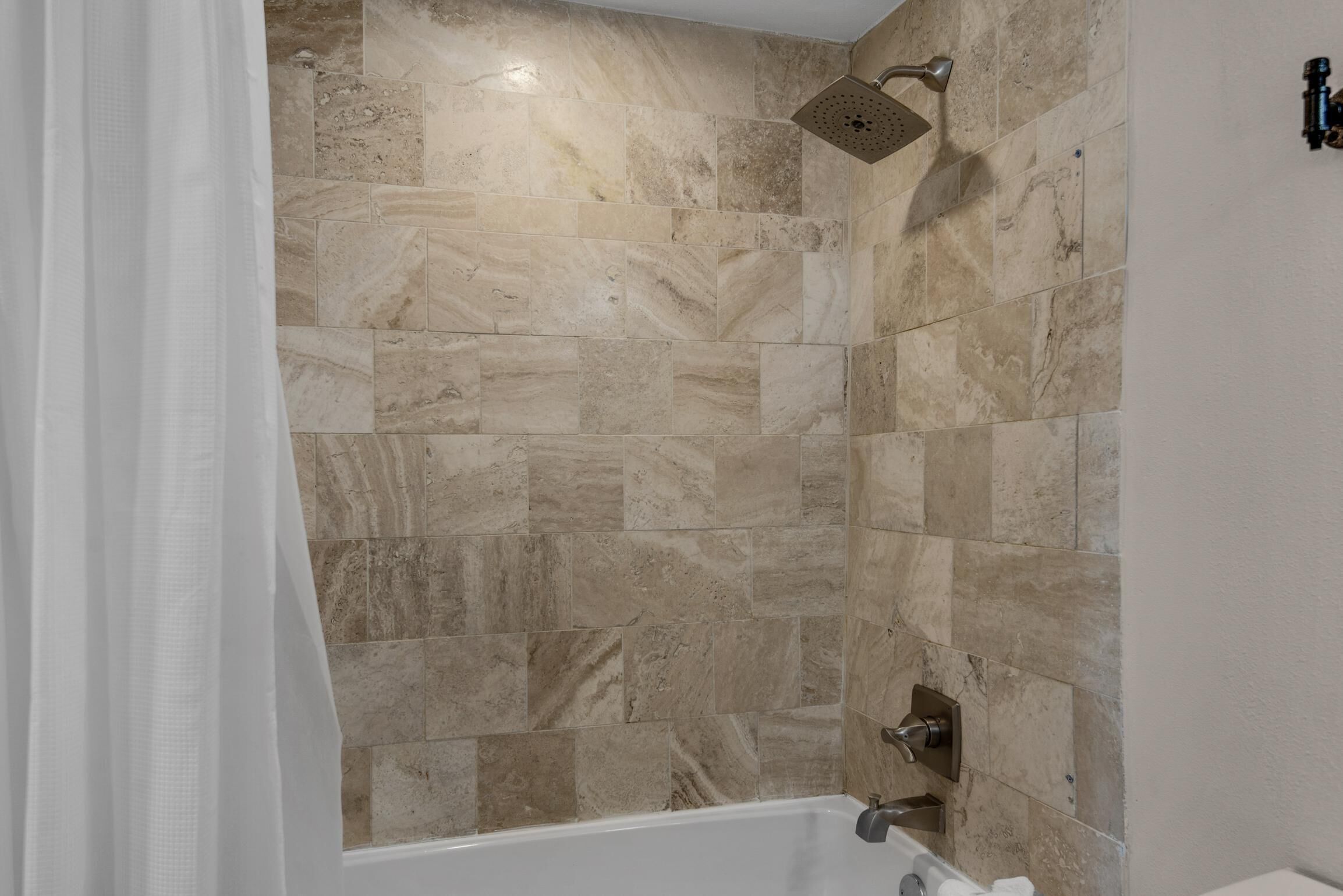 A bathroom with beige marble tiles, a showerhead, and a bathtub.