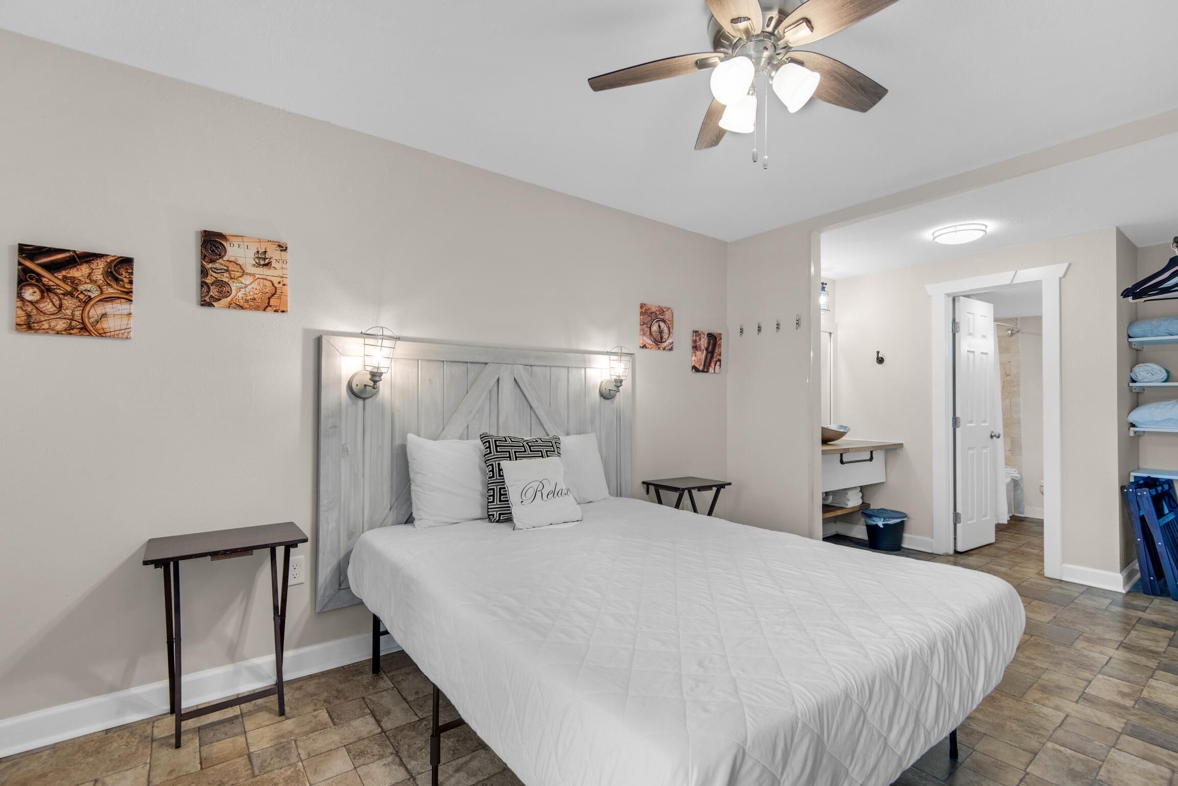 A bedroom with a bed, a bedside table, a ceiling fan, and artwork on the walls.