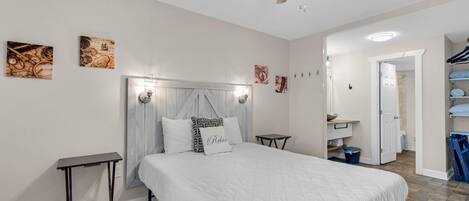 A bedroom with a bed, a bedside table, a ceiling fan, and artwork on the walls.