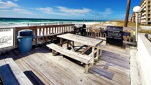 A wooden deck with a picnic table and grill, overlooking a beach with a palm tree and ocean view. - Emerald Isle 302 (Fort Walton Beach)
