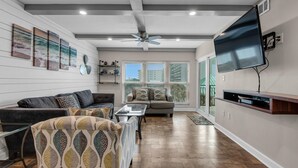 A spacious living room with a large flat-screen TV, two sofas, a coffee table, and a ceiling fan. - Emerald Isle 302 (Fort Walton Beach)