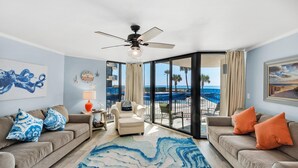 A living room with a large window, a ceiling fan, and a view of the ocean. - Sunbird 102w (Panama City Beach)