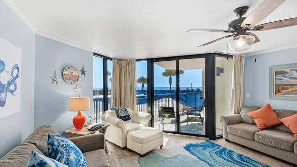 A spacious living room with a view of the ocean, a ceiling fan, and a large window with curtains. - Sunbird 102w (Panama City Beach)