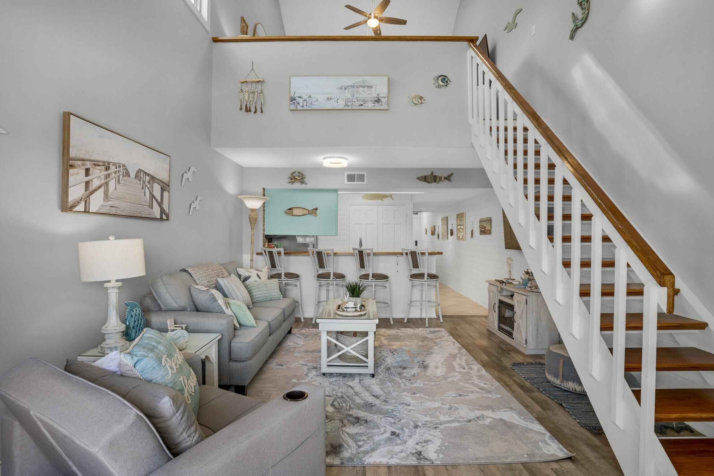A spacious living room with a grey sofa, a coffee table, and a staircase with a wooden railing.