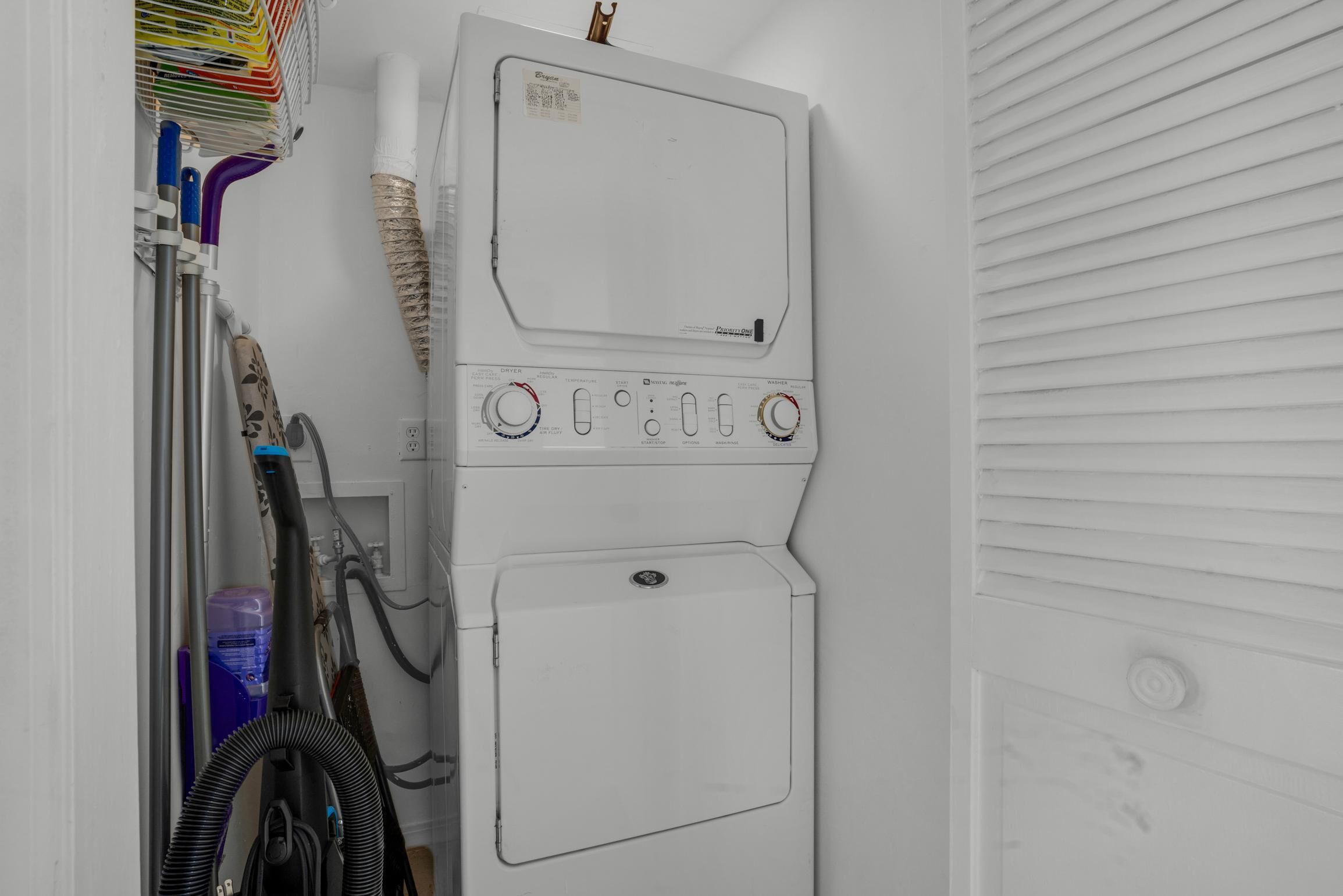 A stacked washer and dryer unit with hoses and a water container.