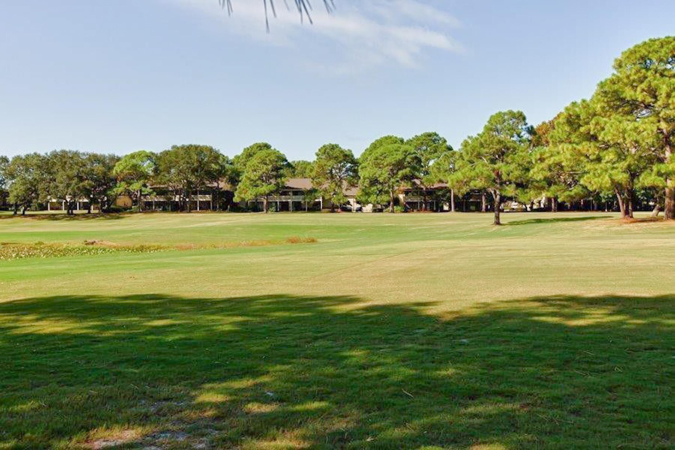 Un campo de golf con un césped cuidado, árboles y edificios al fondo.
