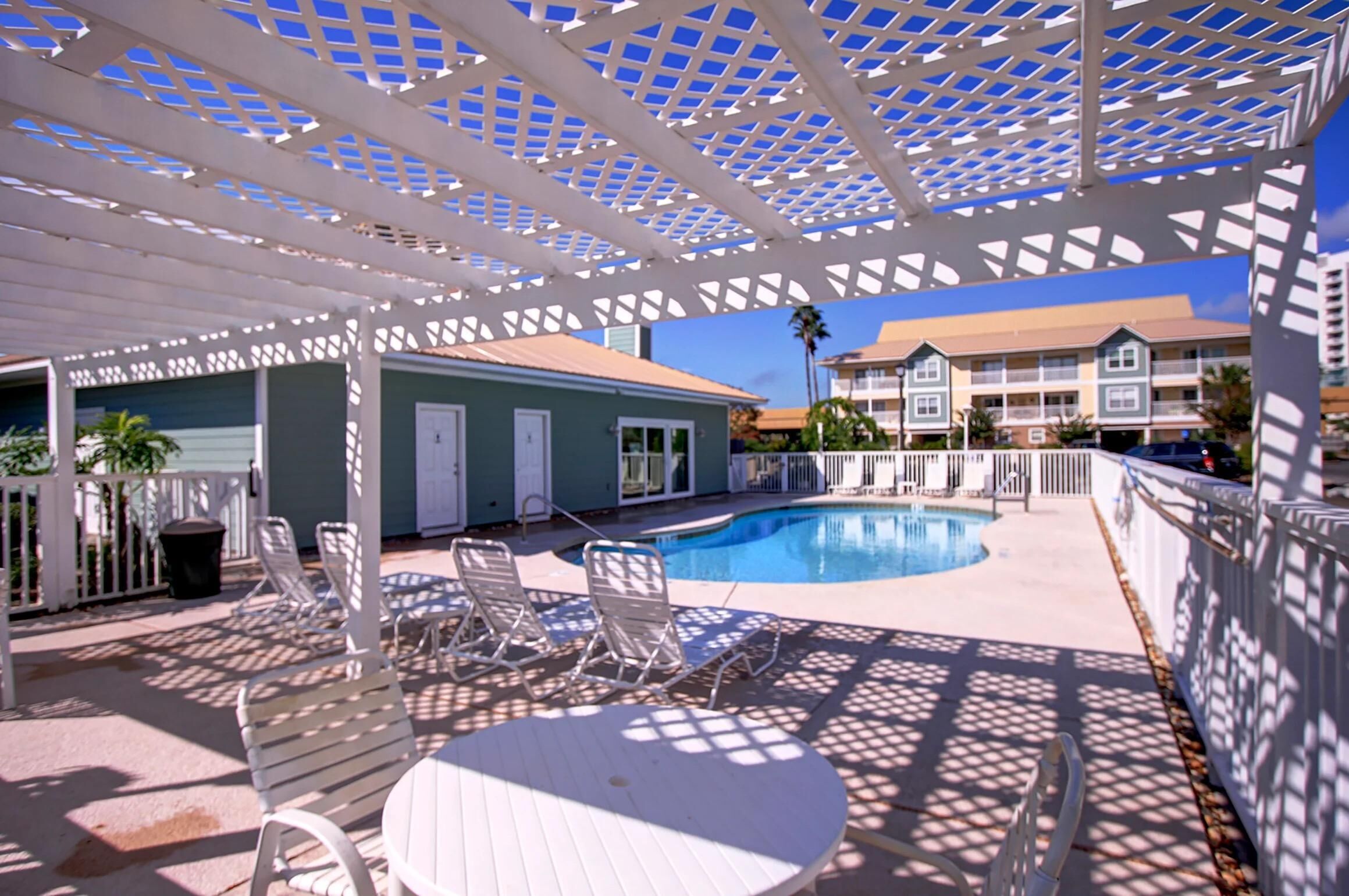 Un espace aménagé au bord de la piscine, avec un patio couvert, des chaises longues et une piscine.