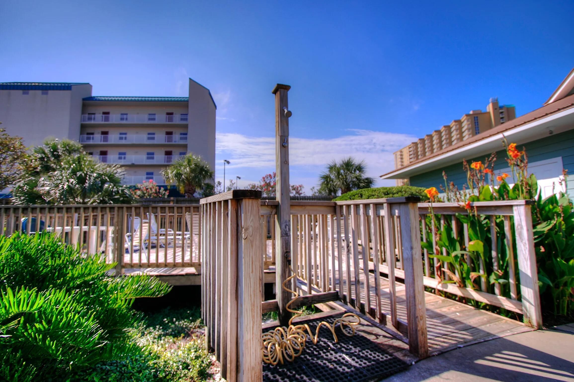 A wooden deck with a rope barrier, surrounded by greenery and a building in the background.