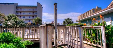 A wooden deck with a rope barrier, surrounded by greenery and a building in the background.