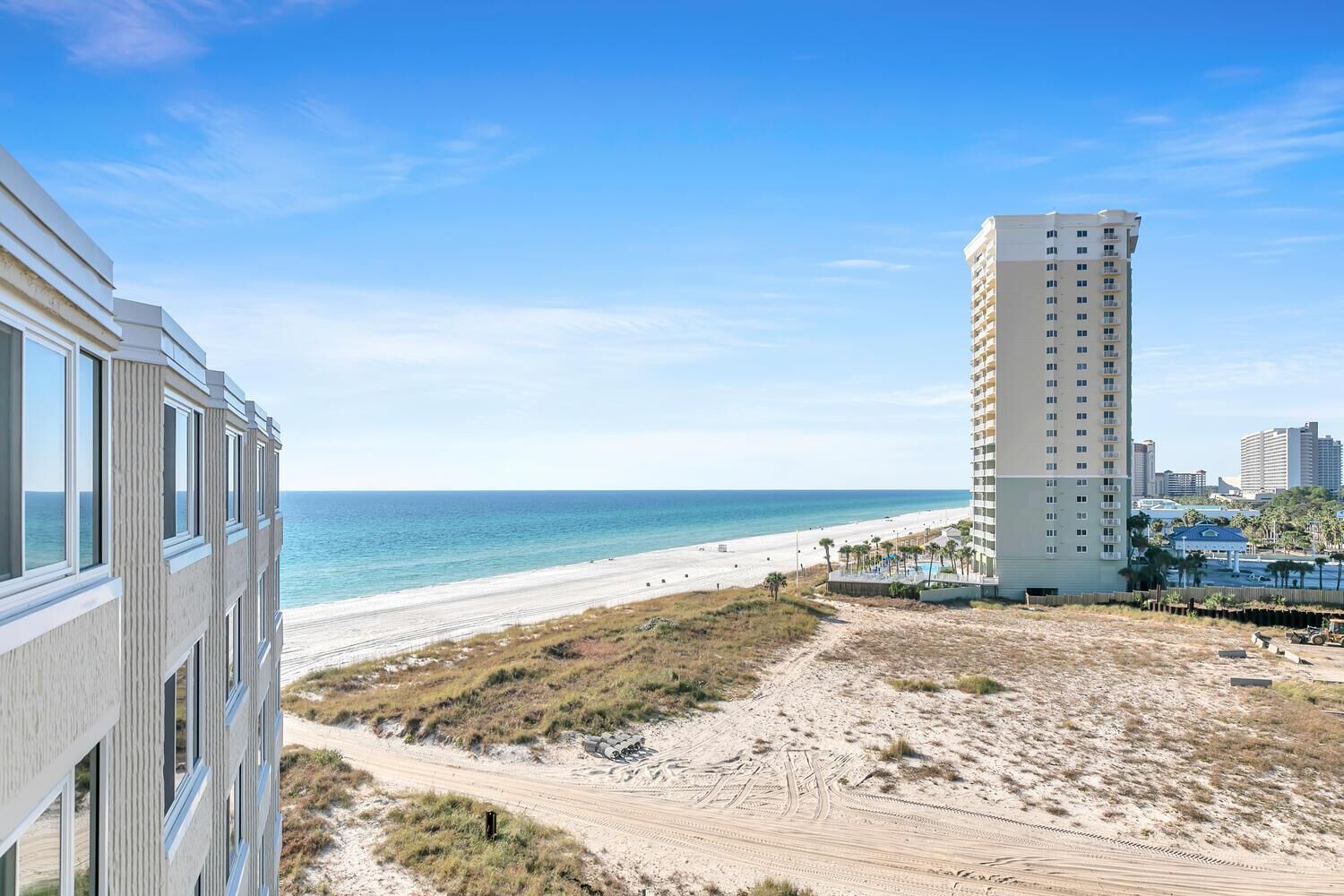 A beachfront hotel with a sandy beach and ocean view, a tall building adjacent to the beach, and a clear blue sky.