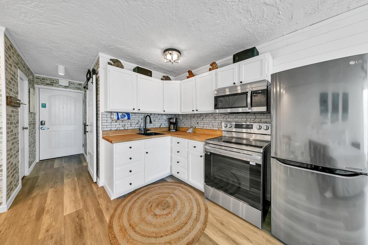 A modern kitchen with white cabinets, stainless steel appliances, and a wooden countertop.