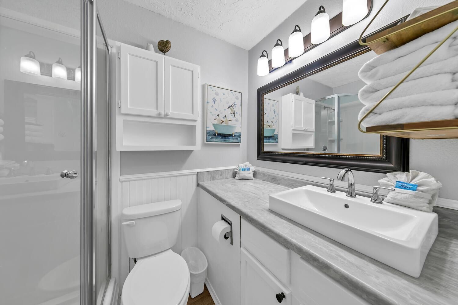 A modern bathroom with a glass shower enclosure, a white toilet, a vanity with a large mirror, and a marble countertop.