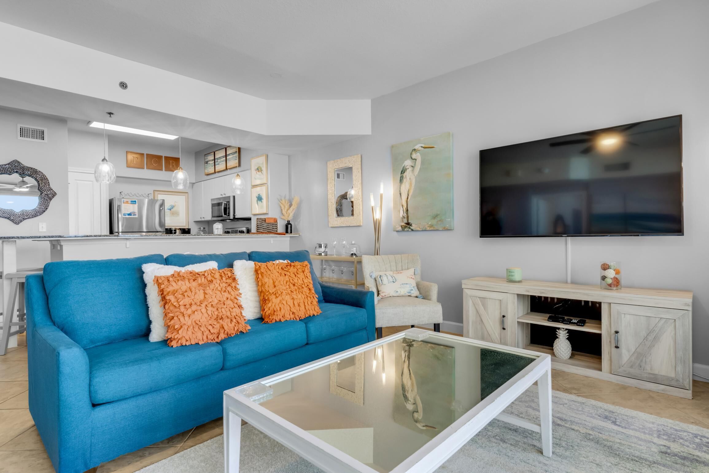 A modern living room with a blue sofa, white coffee table, and a TV mounted on the wall.