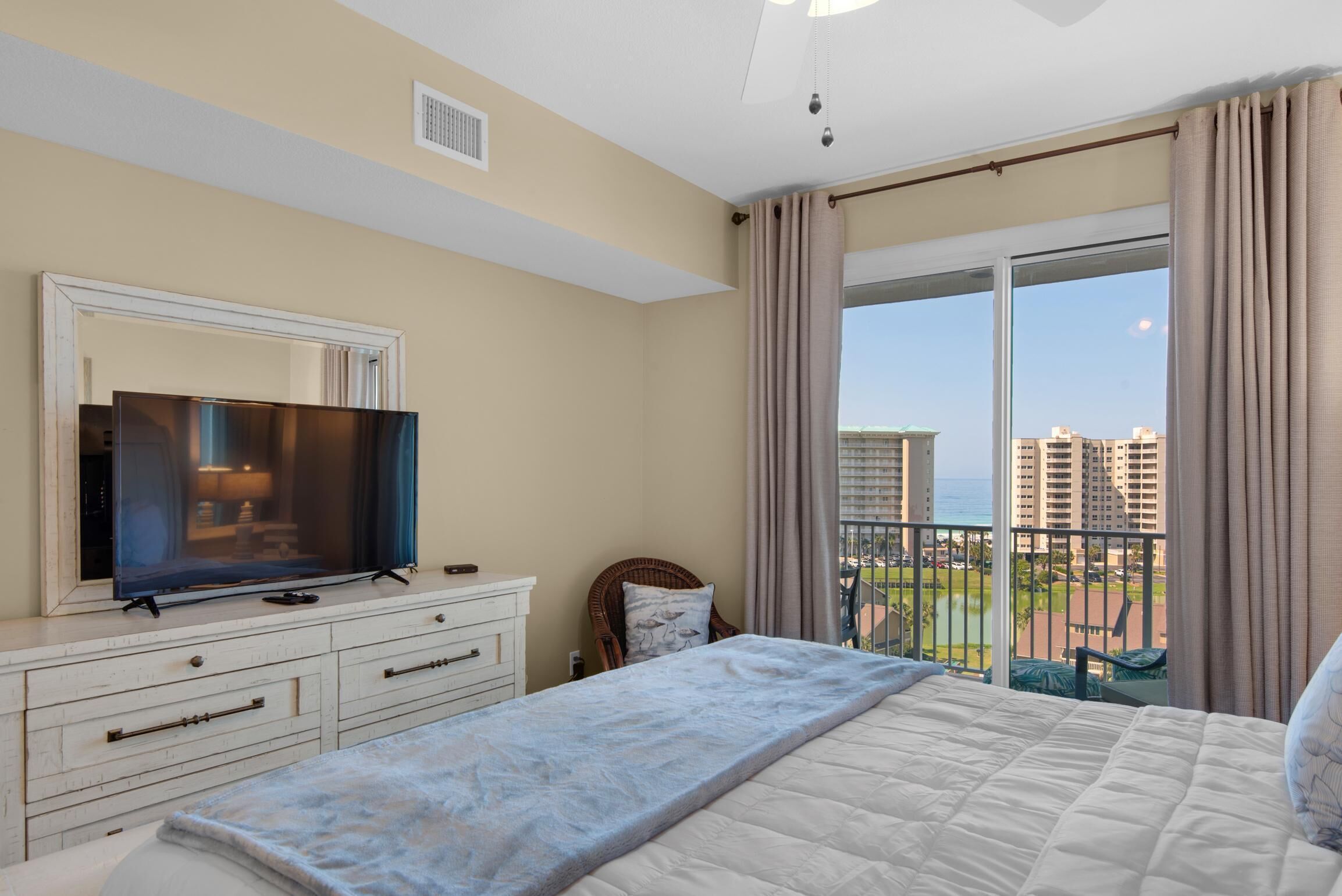 A hotel room with a large bed, a TV on a dresser, a balcony with a view of the city and ocean.