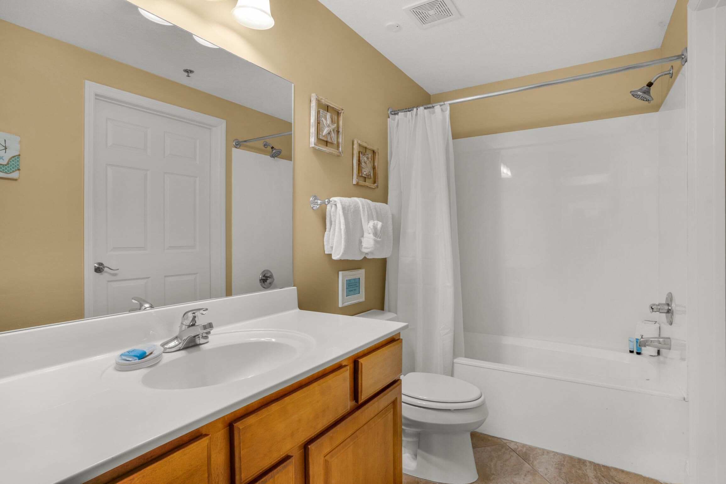 A bathroom with a white sink, vanity, and toilet. There is a shower curtain and a bathtub.