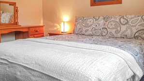 A bedroom with a bed, a bedside table with a lamp, a dresser, and a painting on the wall. - Valley Vineyard Vale (Saundersfoot)