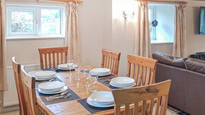 A dining area with a wooden table set for four, chairs, and a sofa in the background. - Valley Vineyard Vale (Saundersfoot)