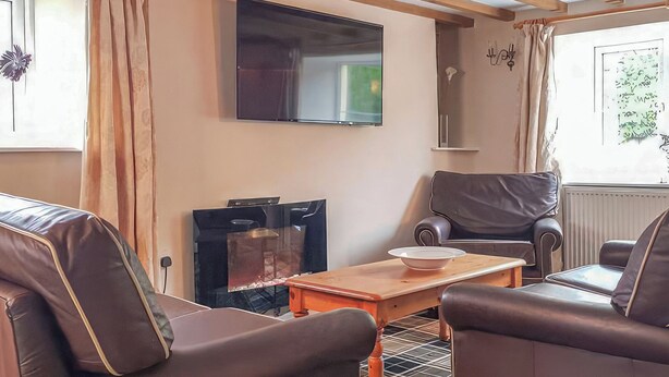 A cozy living room with a fireplace, leather sofas, a TV, and a dining table. - Valley Vineyard Vale (Saundersfoot)
