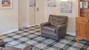 A room with a checkered floor, a leather chair, a wooden cabinet, and wall art. - Valley Vineyard Vale (Saundersfoot)