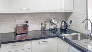 A modern kitchen with white cabinets, a black countertop, a kettle, and a coffee machine. - Valley Vineyard Vale (Saundersfoot)