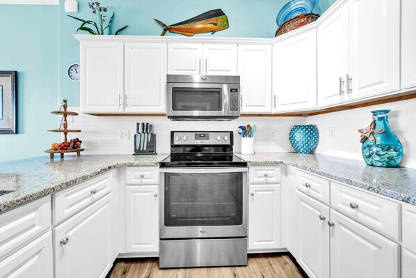 A kitchen with white cabinets, a stainless steel microwave, oven, and granite countertop. - Ocean Villa 2303 (Panama City Beach)
