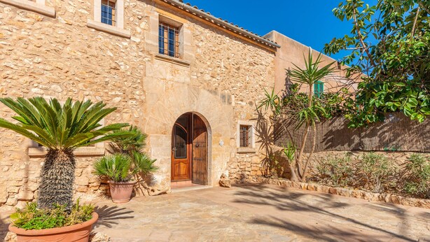 A stone building with a wooden door and arched entrance, surrounded by potted plants and a stone pathway. - S'ALQUERIA ROTJA - Magnificent 17th-century estate with a pool in Santanyí (Santanyí)