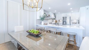 Een moderne keuken met witte kastjes, een groot eiland met een schaal groene appels, en een hangende lamp.