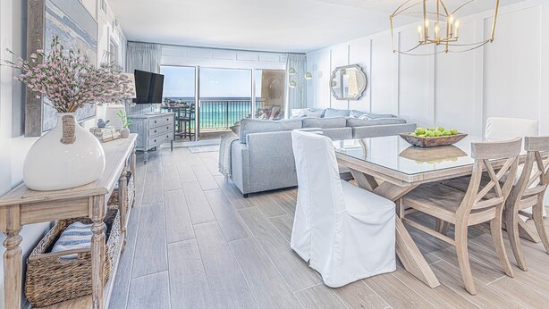 Een moderne woonkamer met een bank, eettafel en stoelen. Er is een televisie en een groot raam met uitzicht op de oceaan.