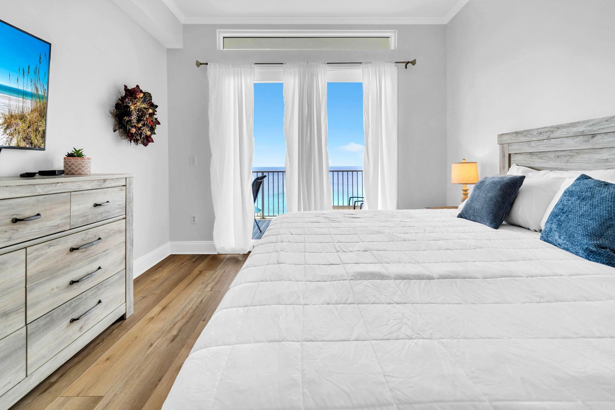 Un dormitorio con cama, cómoda, lámpara, balcón con vistas y un adorno en la pared.
