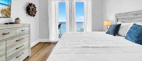 Un dormitorio con cama, cómoda, lámpara, balcón con vistas y un adorno en la pared.