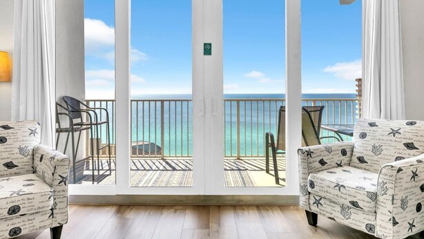 A room with a large sliding glass door leading to a balcony with a view of the ocean. There are two patterned armchairs and a small table on the balcony. - Laketown Wharf Penthouse 2026 (Panama City Beach)