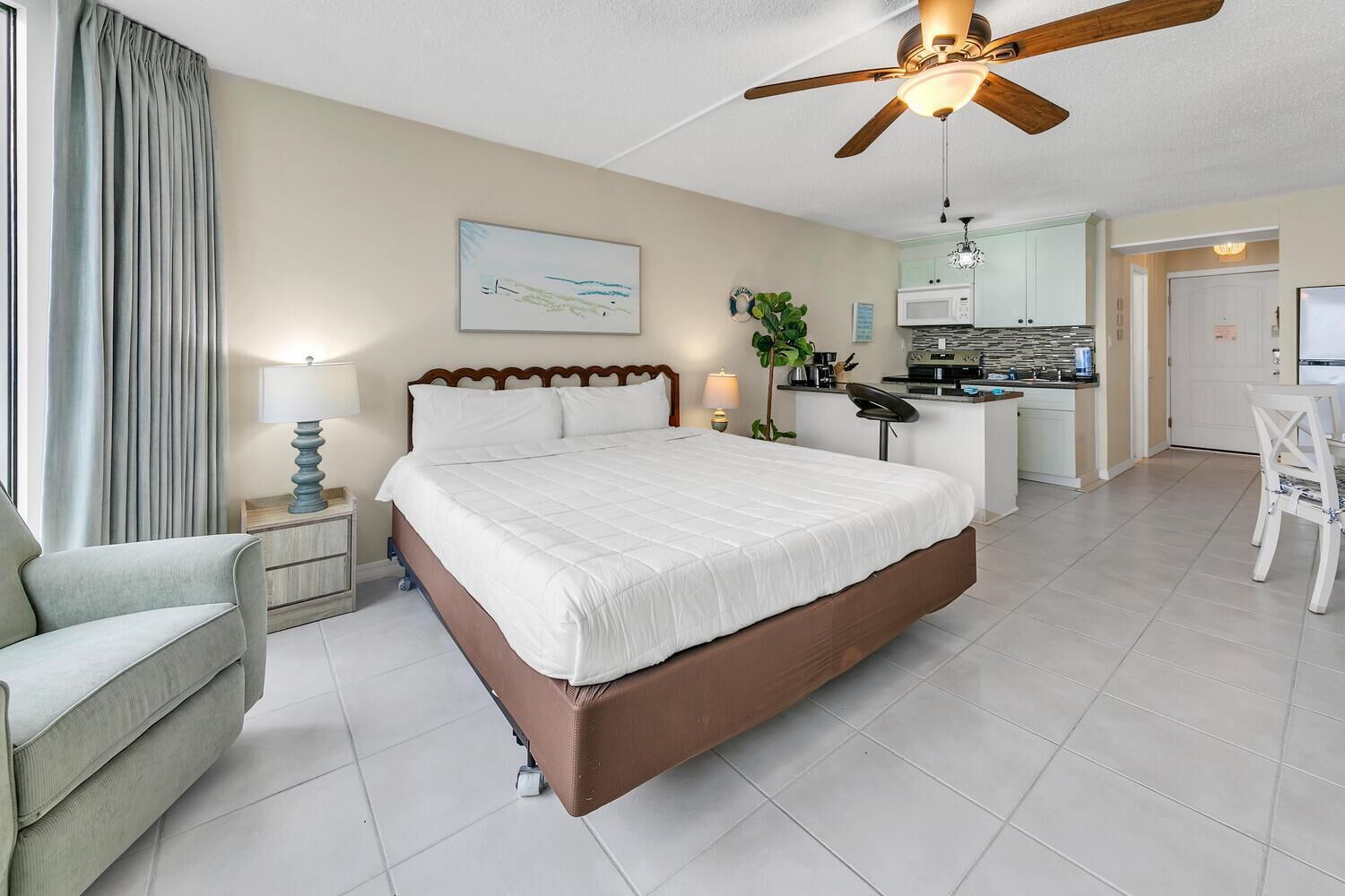 Une chambre d’hôtel avec un grand lit, un bureau, une chaise, une kitchenette et un ventilateur de plafond.