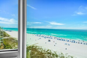 A beach view from a window overlooking a sandy beach with umbrellas and lounge chairs. - Top of the Gulf 825 (Panama City Beach)