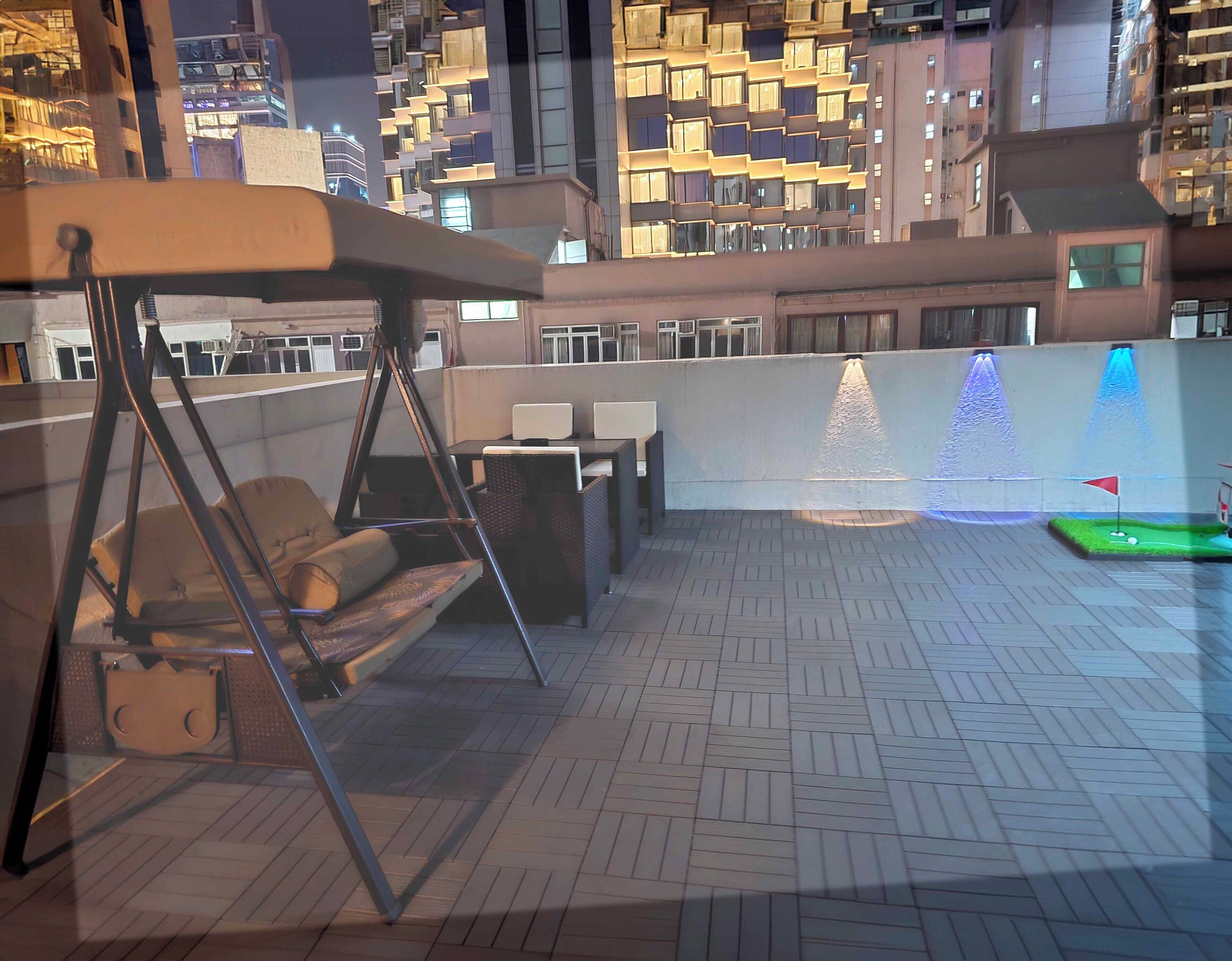 Une terrasse sur le toit avec un fauteuil suspendu, une table et des chaises, ainsi qu’un petit terrain d’entraînement au putting.
