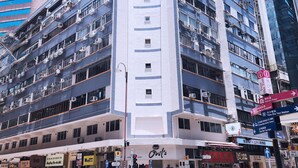 A multi-story hotel with a central white tower, surrounded by other buildings. - Pillows Co-Living (Kowloon)