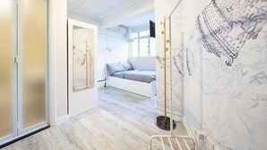 A modern bedroom with a bed, a standing lamp, and a wall-mounted TV. - Pillows Co-Living (Kowloon)